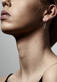 Pendiente de aro de plata con un diseño minimalista, en forma de una delgada media luna. Superficie lisa con un brillo sutil sobre un fondo neutro.