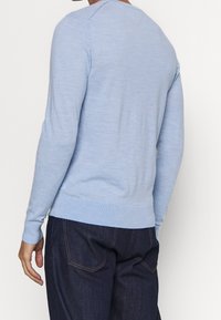 Pull bleu clair en matériau doux, doté de manches longues, de bords côtelés aux poignets et à l'ourlet, et d'un design col rond. Porté avec un jean foncé.