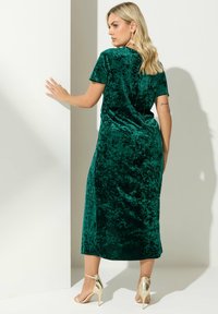 Zielona welurowa midi sukienka z krótkimi rękawami, luźny fason i rozcięciem z boku. Noszona z złotymi szpilkami, podkreślającymi gładką fakturę.