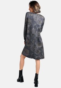 Langärmliges graues Kleid mit einem strukturierten, gemusterten Design mit floralen Motiven, kombiniert mit schwarzen Knöchelstiefeln. Saubere Linien und eine lockere Passform.