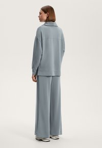 Svetlomodrý oversize sveter a široké nohavice z jemného materiálu. Obsahuje golier a jemné bočné rozparky.