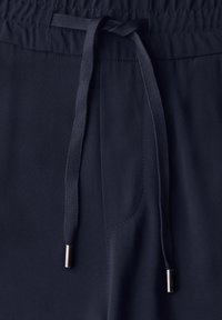 Navy blue joggers with an elastic waistband, adjustable drawstring, and metal-tipped cord. Smooth texture with side pocket detail.