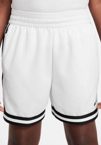 Λευκά αθλητικά σόρτς με μαύρες διπλές ρίγες στο τελείωμα και τις πλευρές, που φοριούνται από άτομο με σκουρόχρωμο δέρμα.