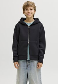 Sweat à capuche noir zippé en tissu doux, avec une poche avant, une capuche réglable et des poignets côtelés, porté par-dessus un t-shirt bleu clair.