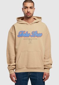 Beige hoodie med en frontlomme, der har et blåt og rødt grafisk tekstdesign. Lavet af blødt stof med ribbede manchetter og bund.