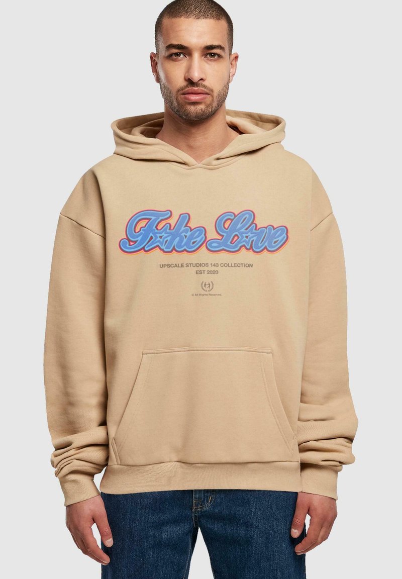 Beige hoodie med en frontlomme, der har et blåt og rødt grafisk tekstdesign. Lavet af blødt stof med ribbede manchetter og bund.