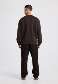 Felpa marrone e pantaloni in corduroy marrone scuro. La felpa presenta un collo rotondo e polsini a costine, mentre i pantaloni hanno tasche posteriori.