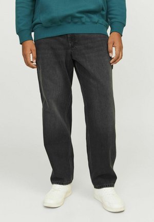 Jeans in denim neri con una vestibilità comoda, caratterizzati da leggere abrasioni e cuciture a contrasto, indossati con sneakers bianche e una felpa teal.