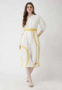 Weißes Hemdkleid mit gelben Akzenten und einem Bindegürtel. Textilstruktur, mittellang und mit Puffärmeln.