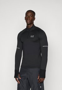 Top de performanță negru cu mânecă lungă, guler cu fermoar până la jumătate, material texturat, accente reflectorizante și deschideri pentru degete în manșete.