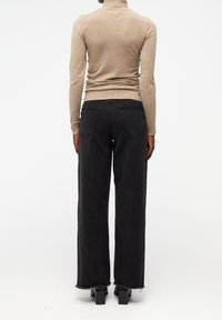 Pull col roulé beige associé à un jean large noir. Le jean présente des ourlets effilochés et deux poches arrière. Texture lisse et design minimaliste.