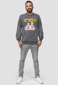 Felpa grigia heather con grafica "Beavis and Butt-Head" sulla parte anteriore, polsini e orlo a costine. Abbinata a jeans grigi chiari e sneakers bianche.