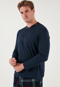 Camisa de manga larga navy con cuello redondo, que presenta un acento a cuadros en el collar y detalles de botones. Tejido suave, corte relajado.