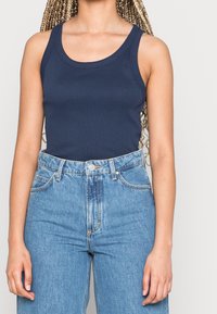 Mörkblå, ärmlös linne i en bomullsblandning, med rund halsringning och en figurnära design, tillsammans med högmidjade denimjeans.