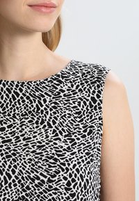 Svart och vit ärmlös klänning med ett strukturerat, abstrakt mönster. Tyget ser slätt ut, med en rund halsringning och skräddarsydd passform.