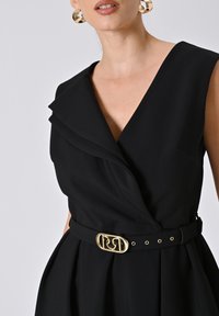 Zwarte jurk met een diepe V-hals en gelaagde kraag, met een getailleerde taille en een gouden logobuckle, die slanke stof en elegant ontwerp combineert.