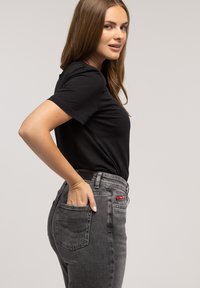 Czarny t-shirt z krótkim rękawem w połączeniu z wysokimi, wyblakłymi szarymi jeansami. Jeansy posiadają boczną kieszeń z czerwonym akcentem. Gładka faktura tkaniny.