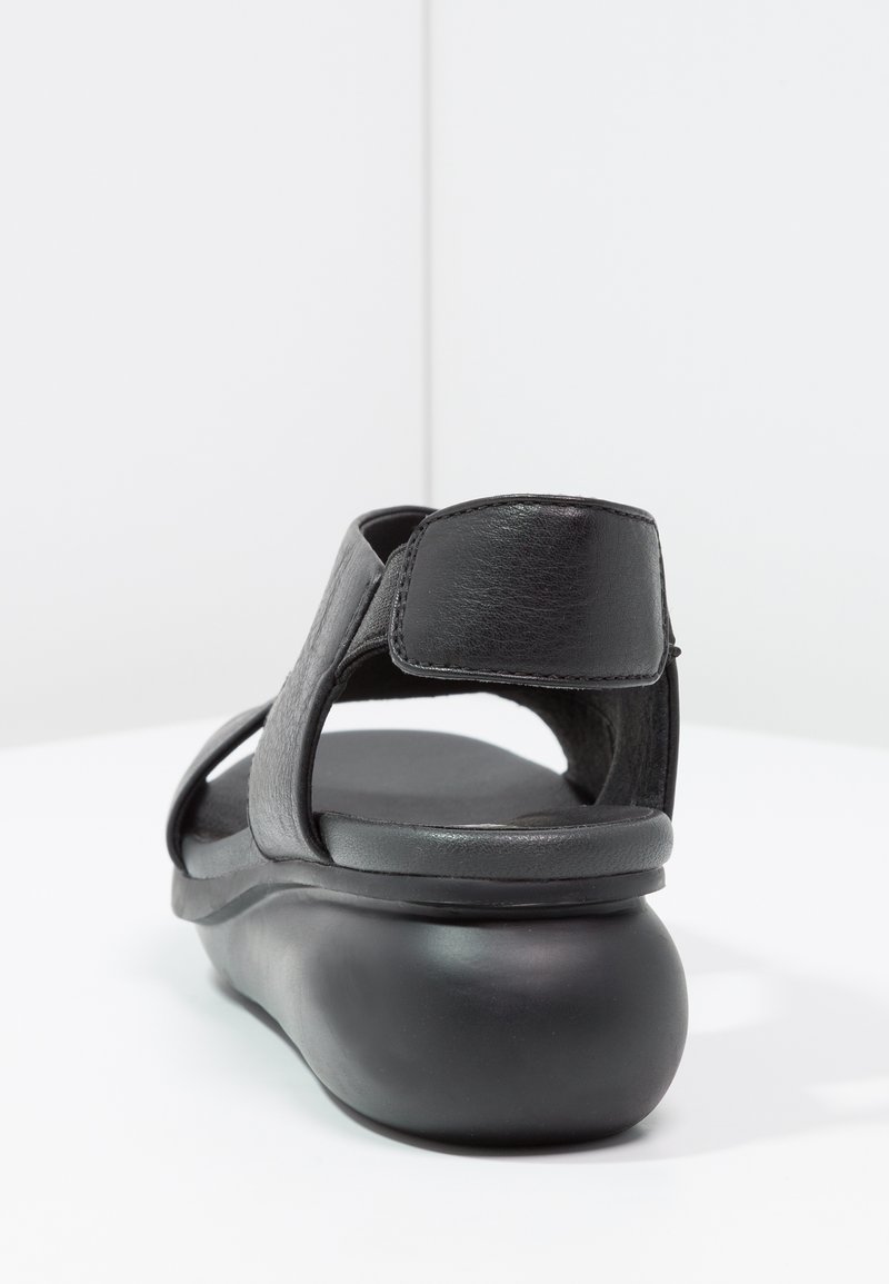 Sandalo in pelle nera con suola arrotondata, schienale aperto e cinturini larghi. Il materiale testurizzato e il design minimalista evidenziano la funzionalità.