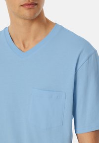 Himmelblaues Baumwoll-V-Neck-T-Shirt mit einer Tasche auf der linken Brust, kurzen Ärmeln und einem lässigen Schnitt. Glatte Textur, einfaches Design.
