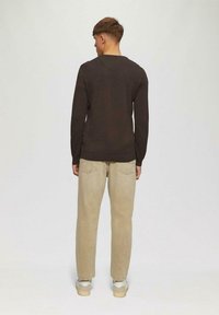 Dunkelbraunes Langarmhemd kombiniert mit hellbeigen Jeans und hellen Sneakern, von hinten auf einem neutralen Hintergrund betrachtet.