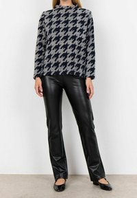 Gebreide trui in grijs met een marineblauw houndstooth-patroon, gecombineerd met glanzende zwarte neplederen broek en zwarte ballerina's.