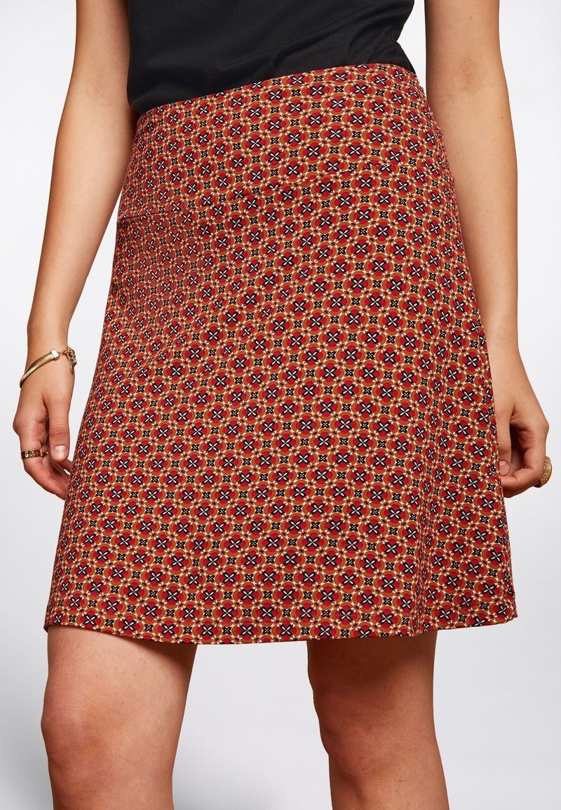 Red patterned skirt with geometric design in shades of orange, black, and white. A-line shape, mid-length, with a smooth woven texture.
