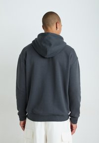 Mørk grå hettegenser med avslappet passform, med hette og ribbestrikkede mansjetter. Laget av mykt stoff, har den et enkelt, minimalistisk design.