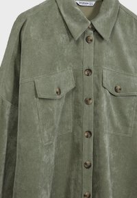 Olive green corduroy shirt jacket with a pointed collar, front button closure, and two chest pockets with rounded brown buttons. Textured fabric.