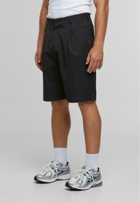 Shorts noirs avec une coupe ajustée, des plis et des poches latérales, associés à des chaussures de sport argentées et bleues et des chaussettes blanches.