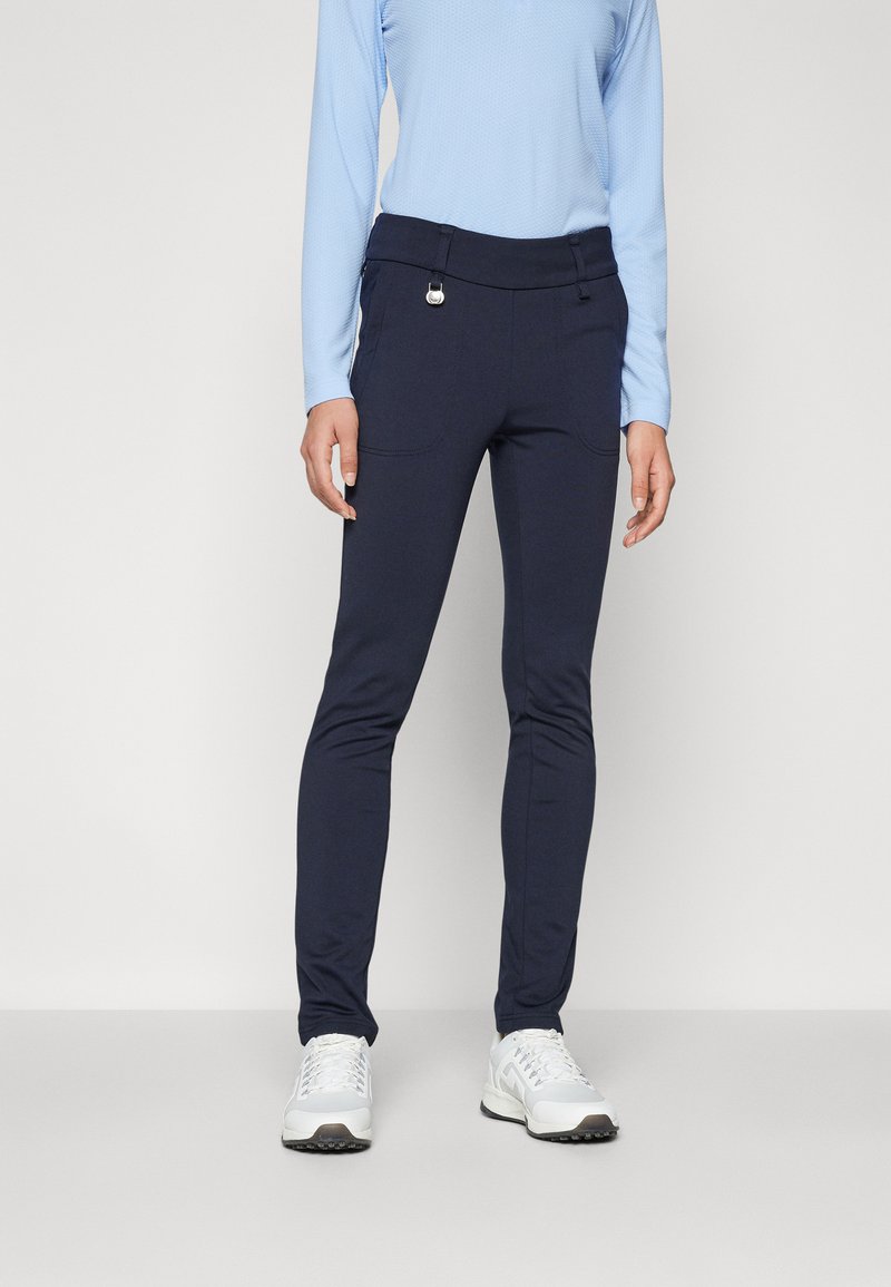 Marineblaue Stretch-Hosen mit glatter Textur, figurbetontem Design, zwei Vordertaschen und einem eleganten Bund, der durch ein rundes Metallelement akzentuiert wird.