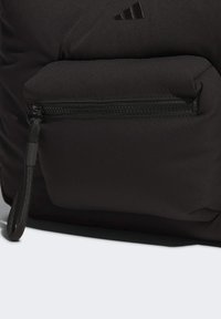 Black padded bag featuring a front zip pocket with a textured zipper pull. Minimalist design with subtle branding in the form of black stripes.