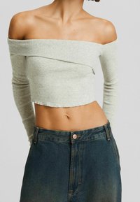 Jasnoszary prążkowany crop top z dekoltem na ramionach i długimi rękawami, zestawiony z ciemnoniebieską spódnicą o wysokim stanie z miedzianym guzikiem.