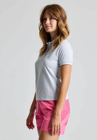 Helles blaues Polohemd mit kurzen Ärmeln und Kragen, kombiniert mit rosa Shorts mit strukturiertem Design und einem Kordelzugverschluss.