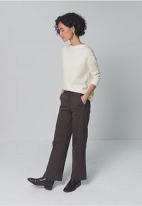 Gebreide trui in crèmekleur, losse pasvorm, gecombineerd met donkerbruine broek met wijde pijpen en zwarte enkelhoge laarzen. Minimalistisch ontwerp, zonder zichtbare patronen.