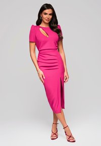 Robe rose ajustée avec de courtes manches bouffantes, découpe en trou de serrure, fente sur le côté et détail froncé sur la jupe. Assortie à des chaussures à talons ouverts à lanières.