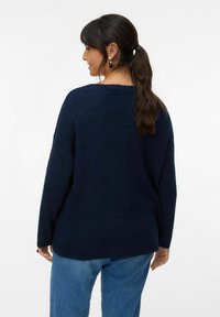 Maglione oversize blu navy con una vestibilità rilassata, texture a coste e spalle scese, abbinato a jeans blu chiaro.