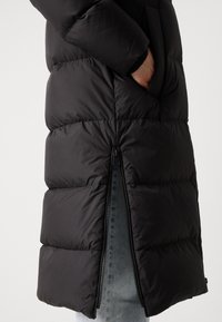 Čierna pufíkova bunda so zipsom na bočnej strane, so prešívaným dizajnom a hladkým, lesklým povrchom.