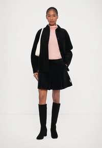 Črn žametni jopič in krilo, roza turtleneck, črne škornje do kolen; krilo ima gube, torba je smetano bela.