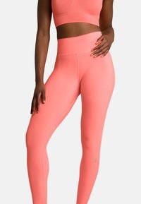 Korale legginsy do ćwiczeń z wysokim stanem, gładką fakturą i detalami na szwach bocznych. Zawierają logo w pobliżu kostki.