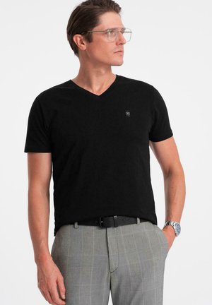 T-shirt nera a maniche corte con scollatura a V in tessuto morbido, con un piccolo logo sul petto, abbinata a pantaloni grigi a quadri.