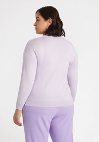 Lilafarbener Pullover mit langen Ärmeln, rundem Hals und geripptem Saum. Weiche Textur, getragen mit passenden lilafarbene Hose. Einfaches und minimalistisches Design.