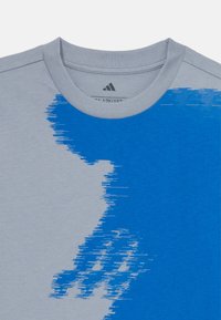 Szary T-shirt z niebieskim gradientem, z okrągłym dekoltem i miękką fakturą. Prezentuje abstrakcyjny wzór na obszarze klatki piersiowej.