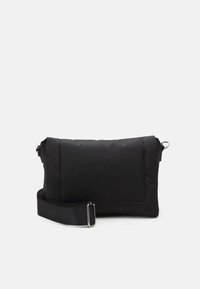 Black nylon bag with a rectangular shape, padded texture, flap closure, and adjustable strap. Features a visible exterior pocket.