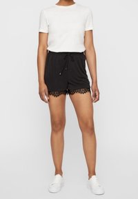 Shorts noirs avec une bordure en dentelle, taille élastique avec cordon de serrage, associés à un t-shirt blanc à manches courtes et des baskets blanches. Tissu lisse, design décontracté.