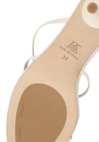 Semelle d'une sandale en cuir beige taille 37 avec de fines lanières blanches et détails de la marque "Kazar Studio" et "Cuir Véritable".