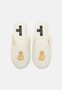 Biele šľapky na slip-on s jemnou textúrou, so zlatou vyšívanou monogramovou a korunkovou výšivkou, označené "LAUREN" na čiernych visačkách.