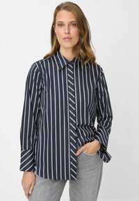Camicia a righe navy con bottoni, righe verticali, colletto a punta e maniche lunghe. Presenta un dettaglio a strisce diagonali sottili a contrasto su un lato.