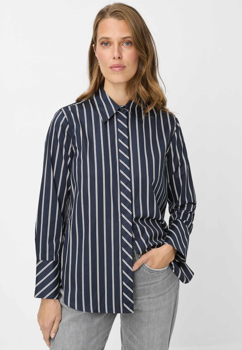 Camicia a righe navy con bottoni, righe verticali, colletto a punta e maniche lunghe. Presenta un dettaglio a strisce diagonali sottili a contrasto su un lato.