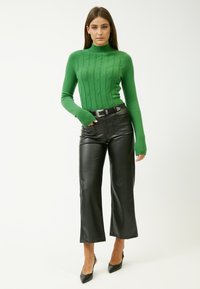 Grüner gestrickter Rollkragenpullover mit Zopfdetails, kombiniert mit schwarzen Leder-Culottes und schwarzen spitzen Absätzen.
