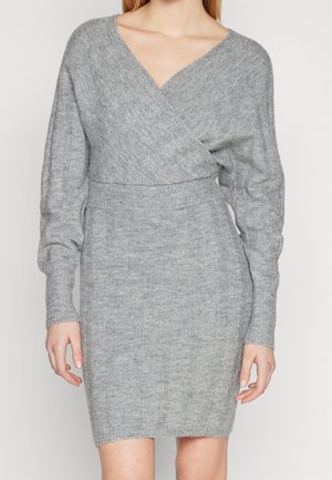 Femme portant une robe en maille gris clair ajustée avec des manches longues et un corsage style portefeuille en V.